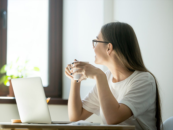 A young person able to relax with a cup of tea in front of their laptop at home.