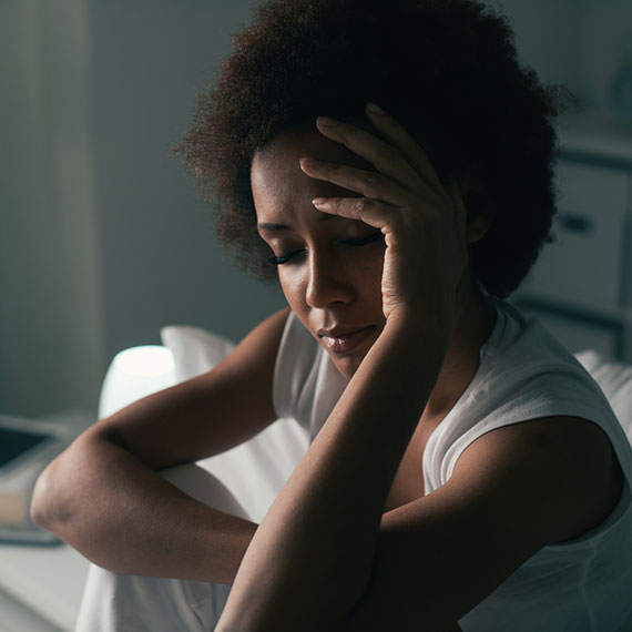 A woman holds her forehead, eyes closed, while sitting up in bed.