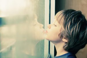 "Autism Spectrum Disorder (ASD)". A child looks out the window while leaning their chin on the glass.