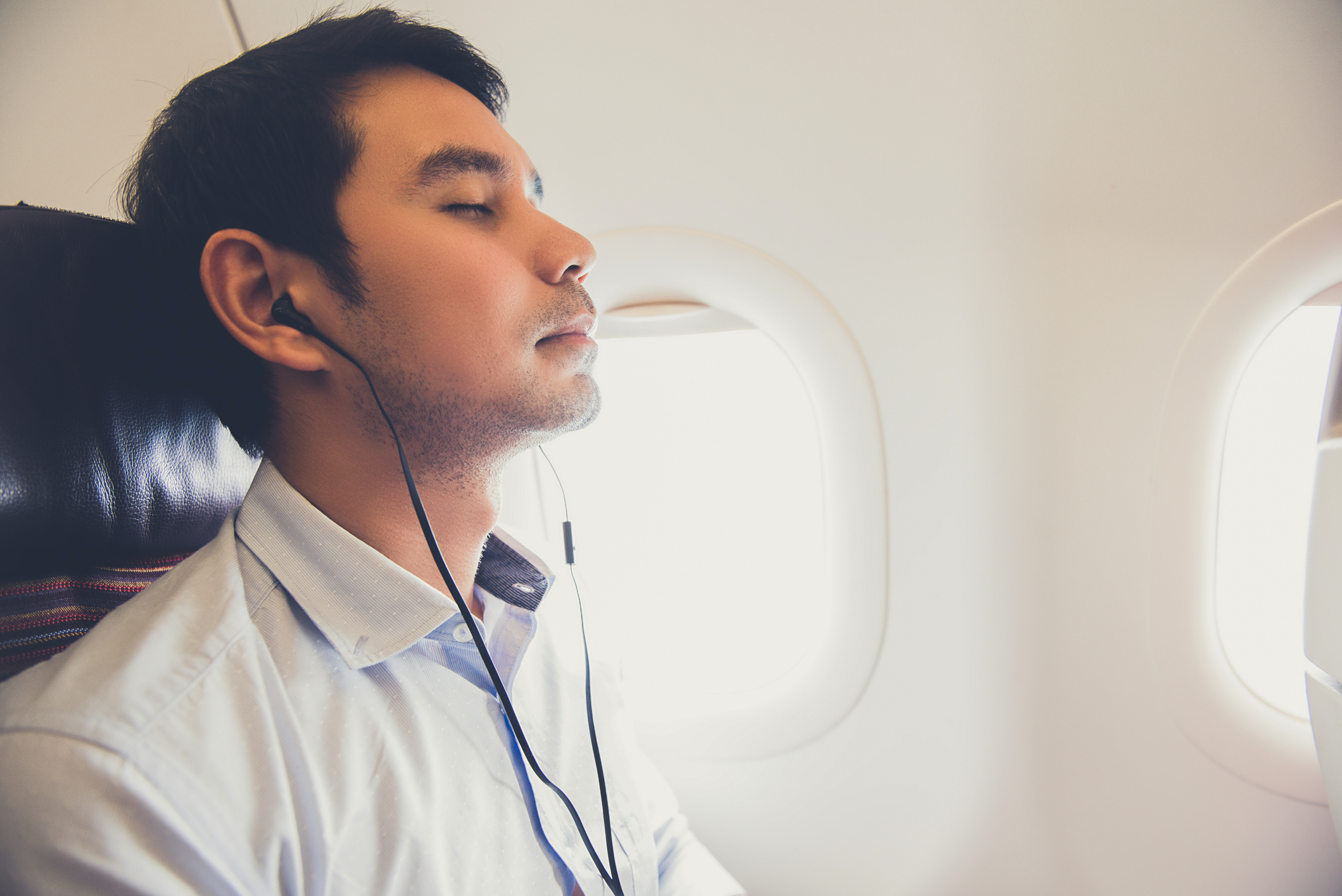 "Panic attack treatment". Young man relaxing with headphones with eyes closed during a flight.