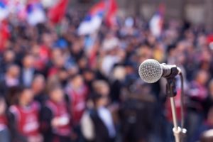 "Performance anxiety". Focus on a microphone with a crowd out of focus in the background.