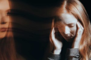 "Psychosis". Out of focus images of a woman holding her temples and looking on at herself.