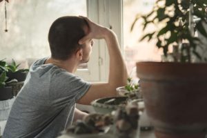 "Post-traumatic stress disorder (PTSD)". A young man with a shaved head sits near a number of plants, and looks out the window with his hand on his forehead.