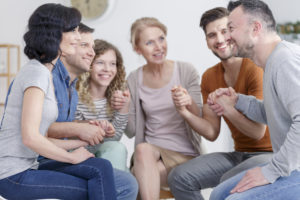 Group therapy participants holding hands in a circle supporting each other.