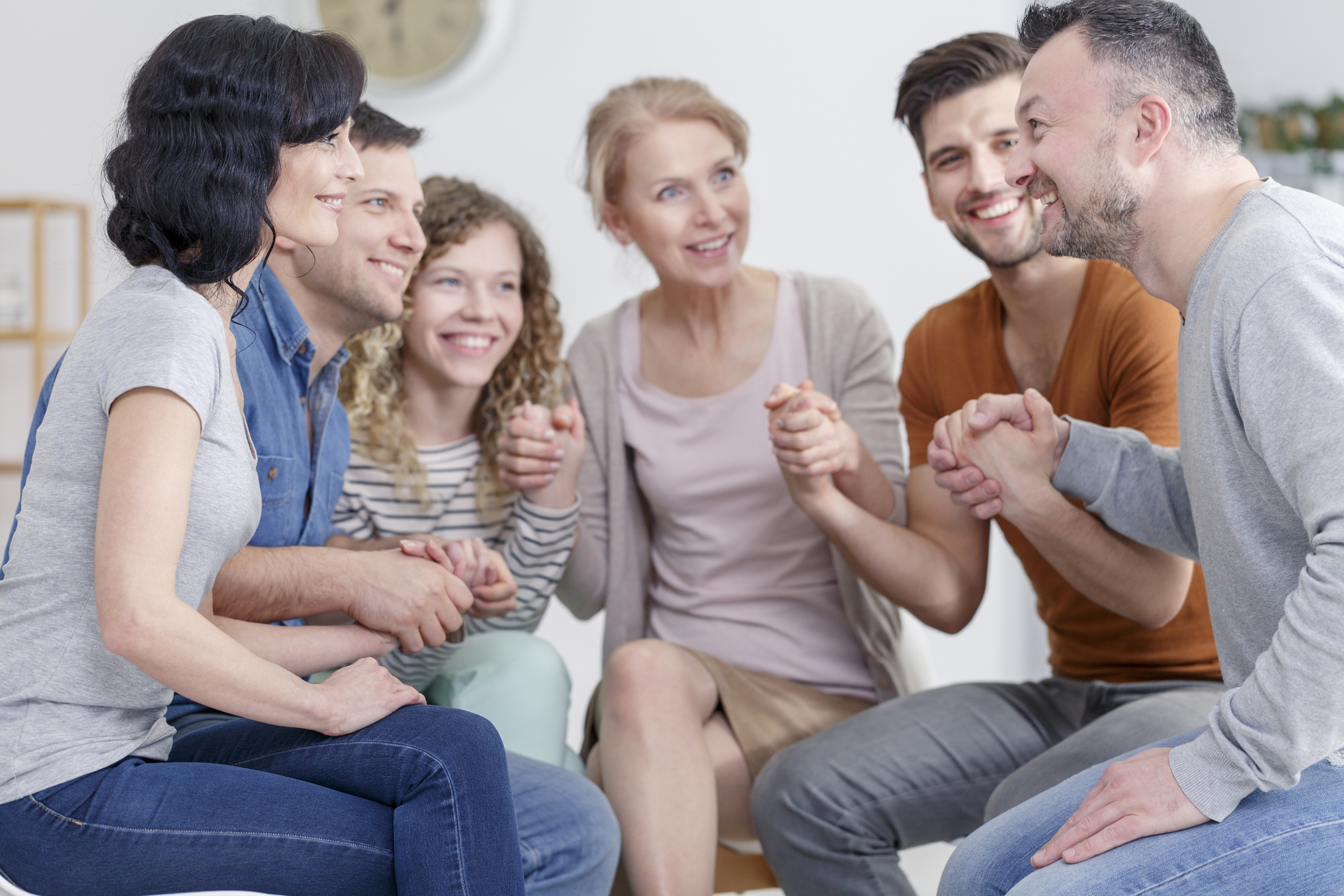 Group therapy participants holding hands in a circle supporting each other.