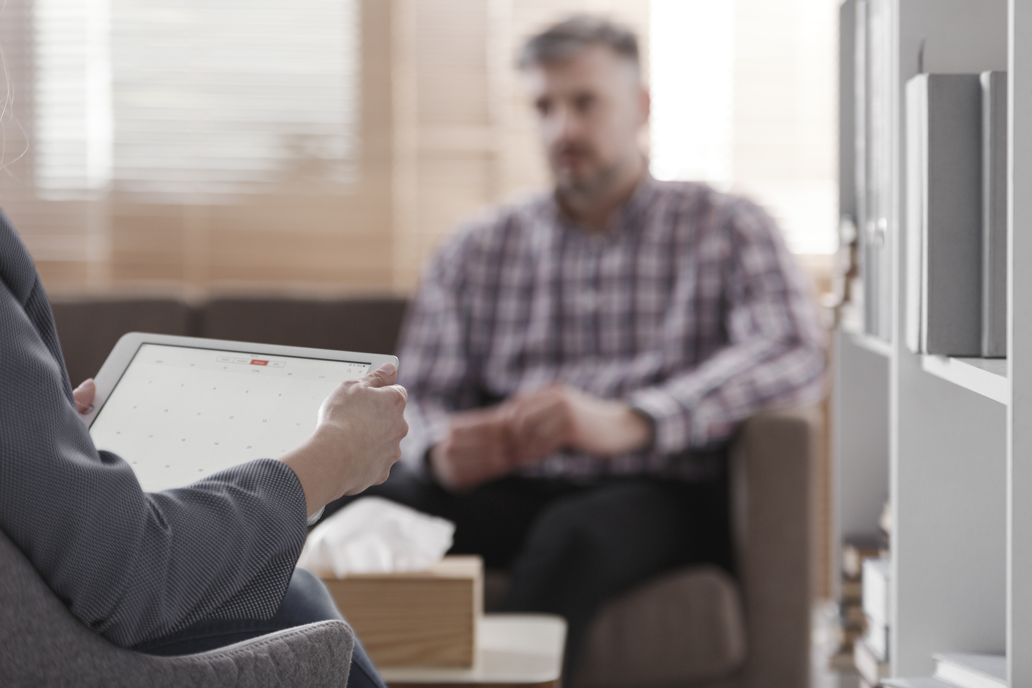 A middle-aged man in a psychotherapy session while a psychiatrist holds a tablet.