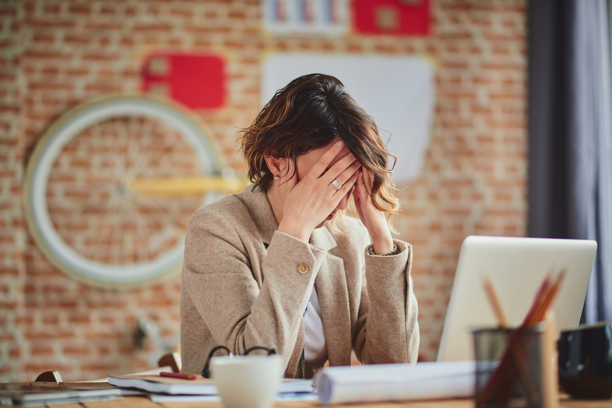 A woman stressfully clutching her head in her hands while at work in a modern office.