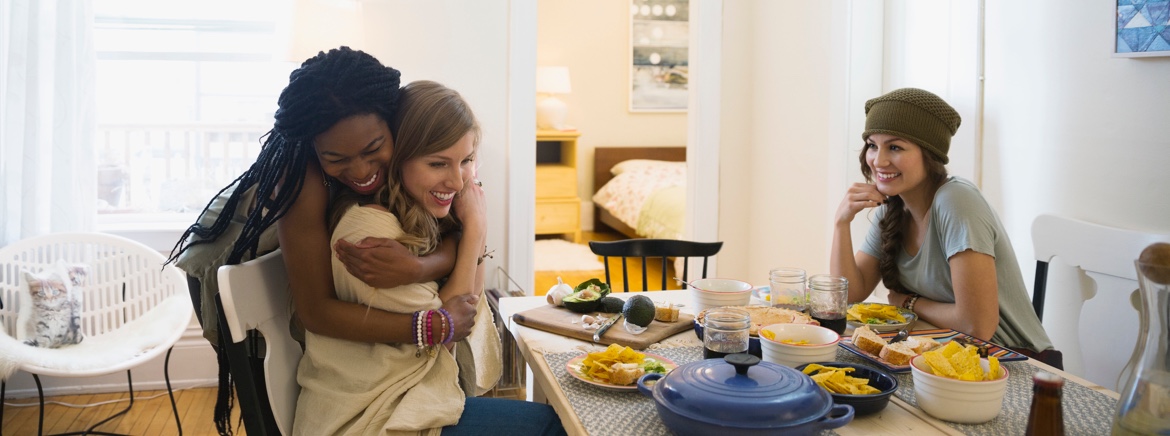 "Treatment for eating disorders". A young woman hugs her roommate while everyone sites down to a healthy homecooked meal.