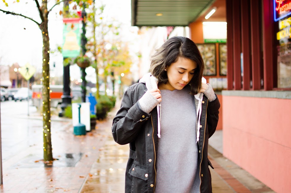 Young woman adjusts her hooded jacket on a rainy autumn street while gazing down..