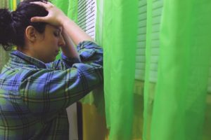 "Anger Management". An exasperated woman leans against a wall, holding her head in both hands.