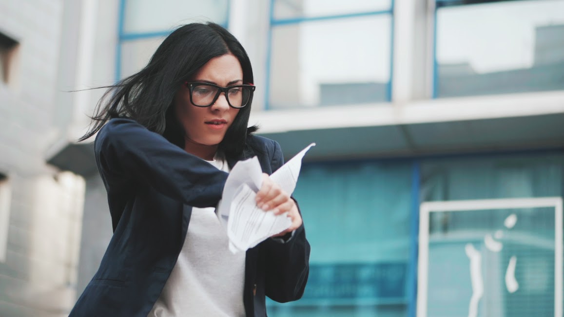 An angry businesswoman tears up some paper while walking.