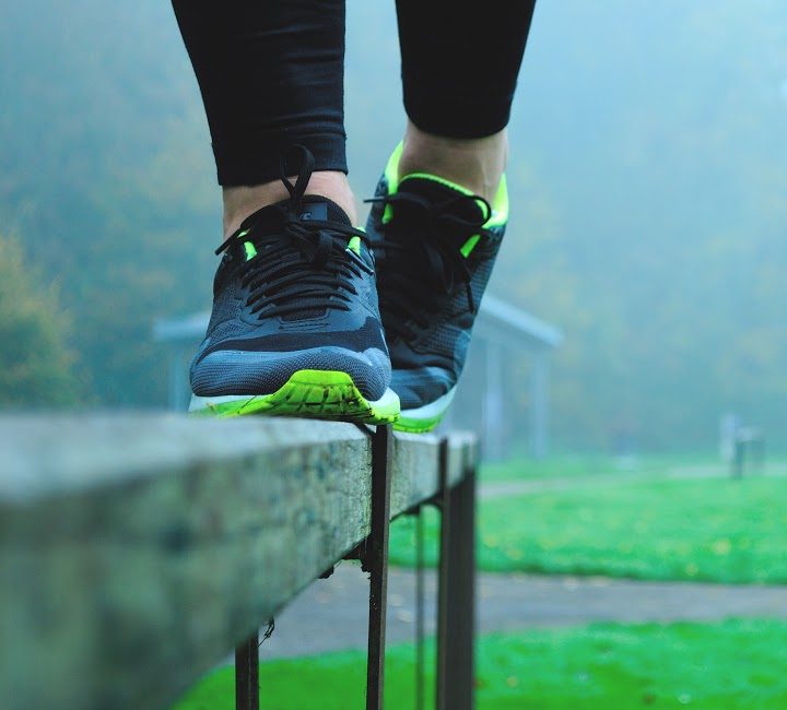 Close-up of running shoes while someone balances on a fence in a misty park with a track.