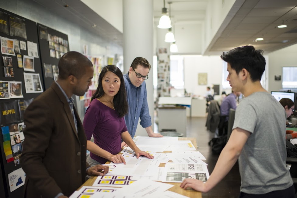 A diverse team in a modern workplace discussing a proposal spread out on a table.