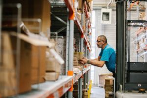 "Panic". A middle aged man picking up items from a shelf in a warehouse.