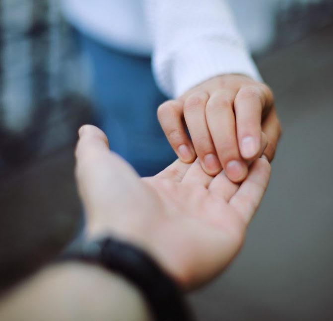 A helping hand holding someone's outstretched fingertips.