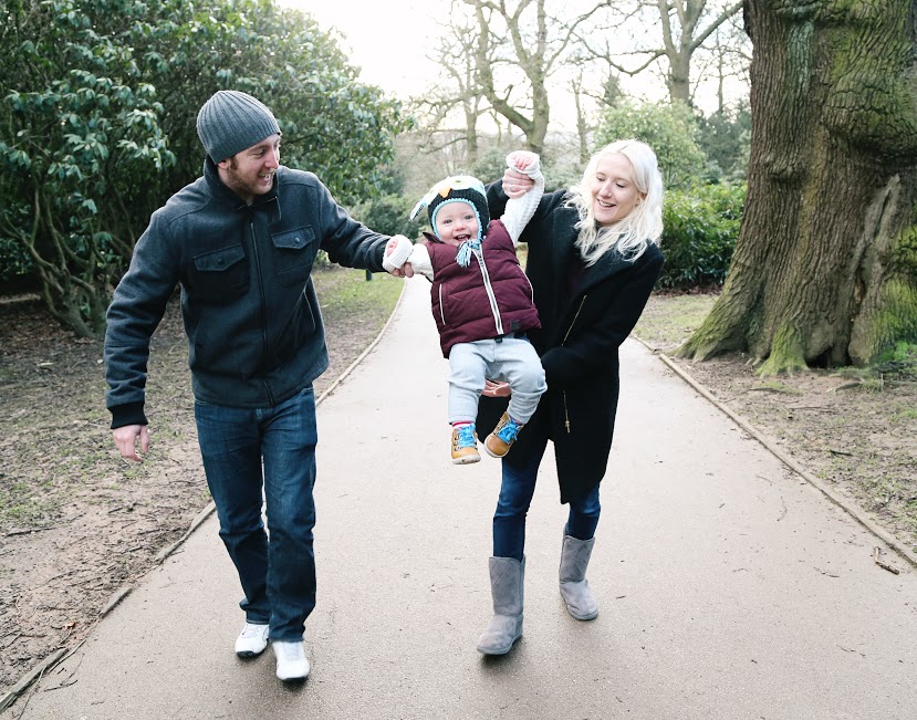 Young couple happily swinging their toddler into the air while walking along a wooded path.