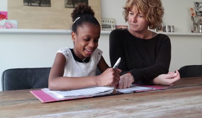 A woman helps a smiling child with her homework.